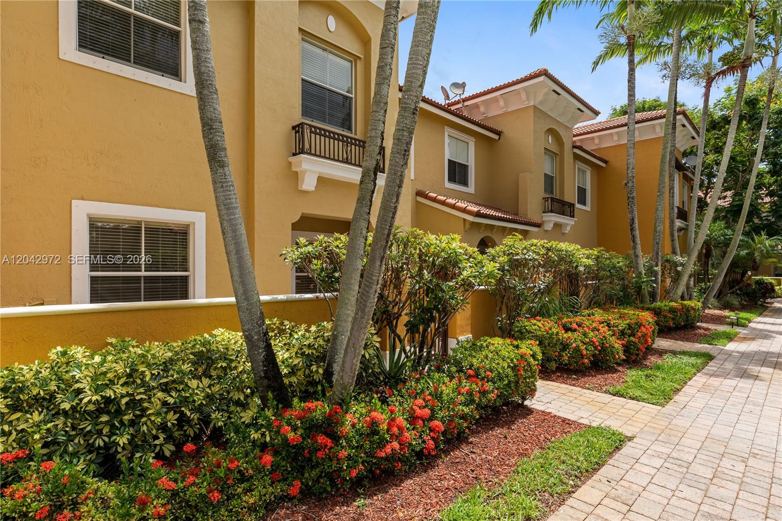 The exterior of a two-story tan stucco building features palm trees and landscaped flower beds — 3405 Merrick Ct # 1209, Margate FL 33063, MARGATE, FL