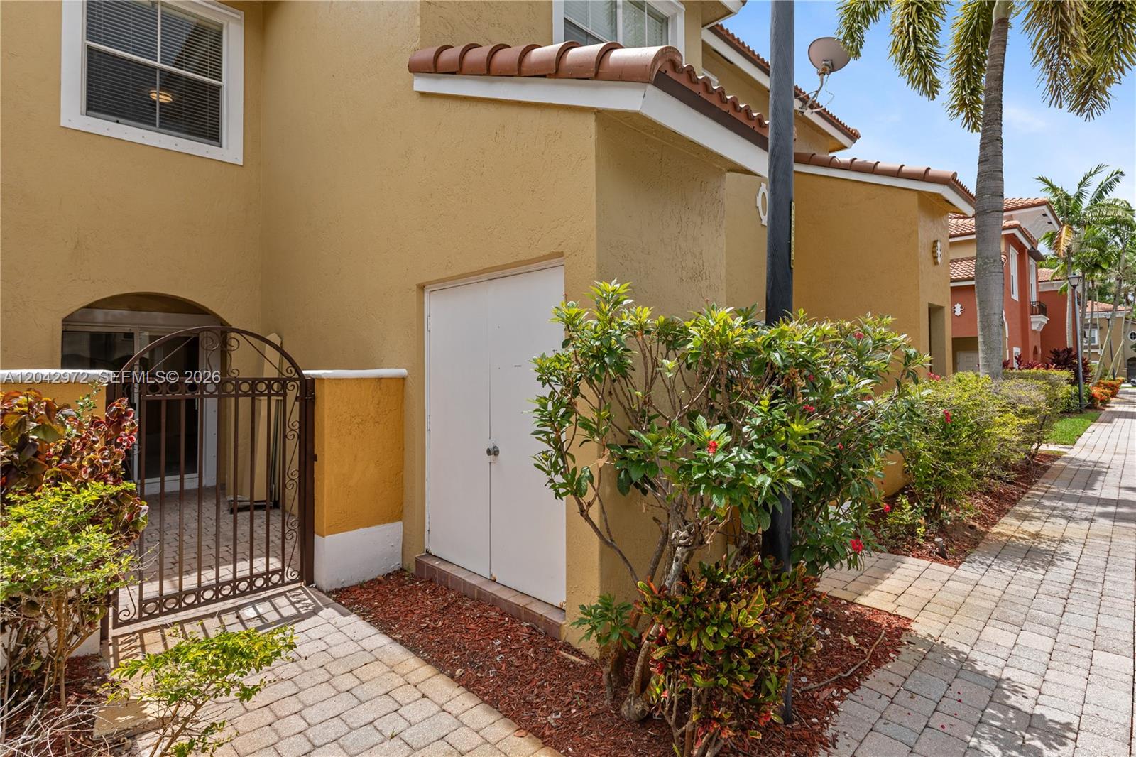The exterior of a tan stucco townhouse features a gated courtyard and a storage closet — 3405 Merrick Ct # 1209, Margate FL 33063, MARGATE, FL