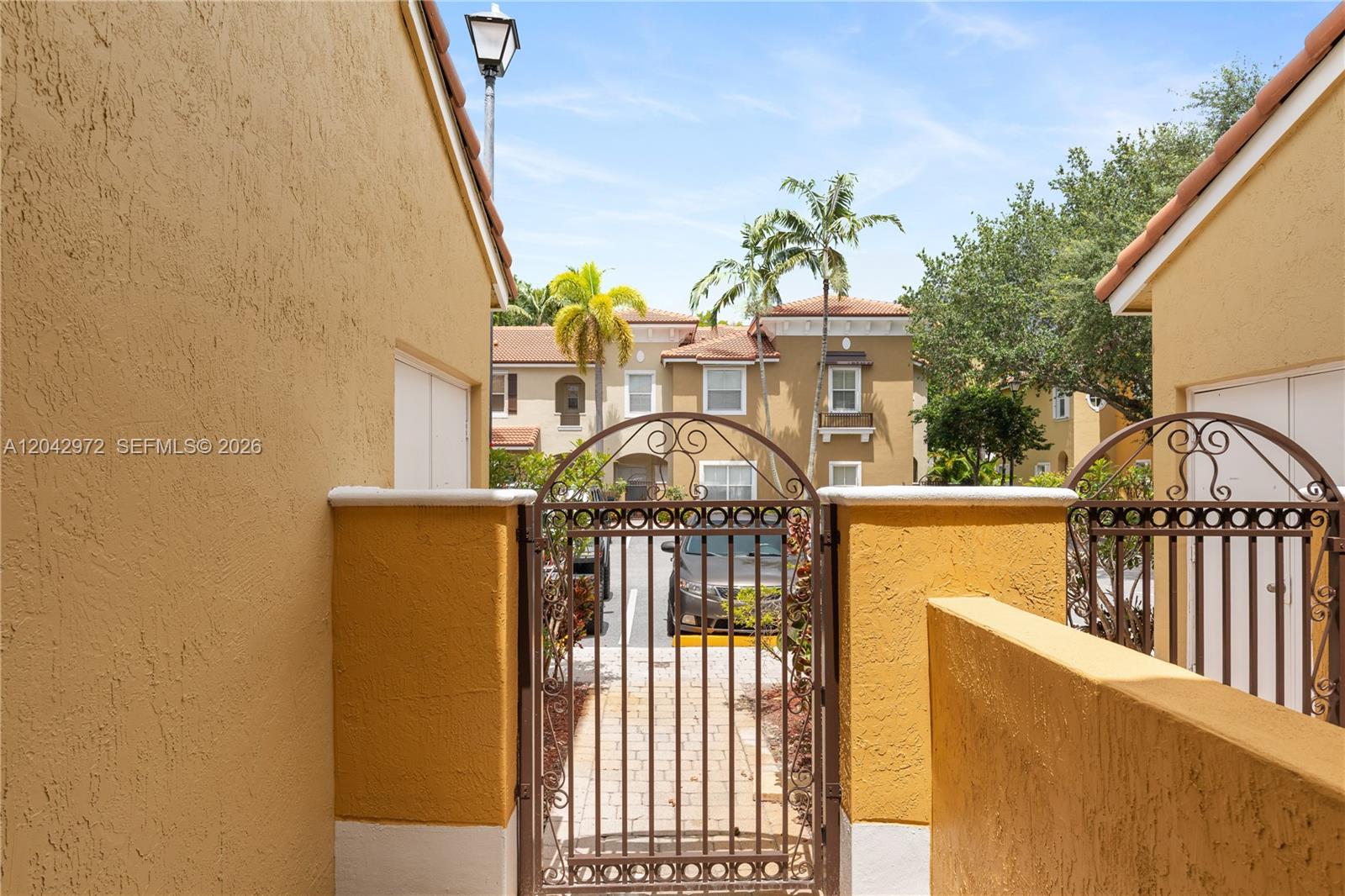 A metal gate stands between two stucco walls leading to a parking area and buildings — 3405 Merrick Ct # 1209, Margate FL 33063, MARGATE, FL