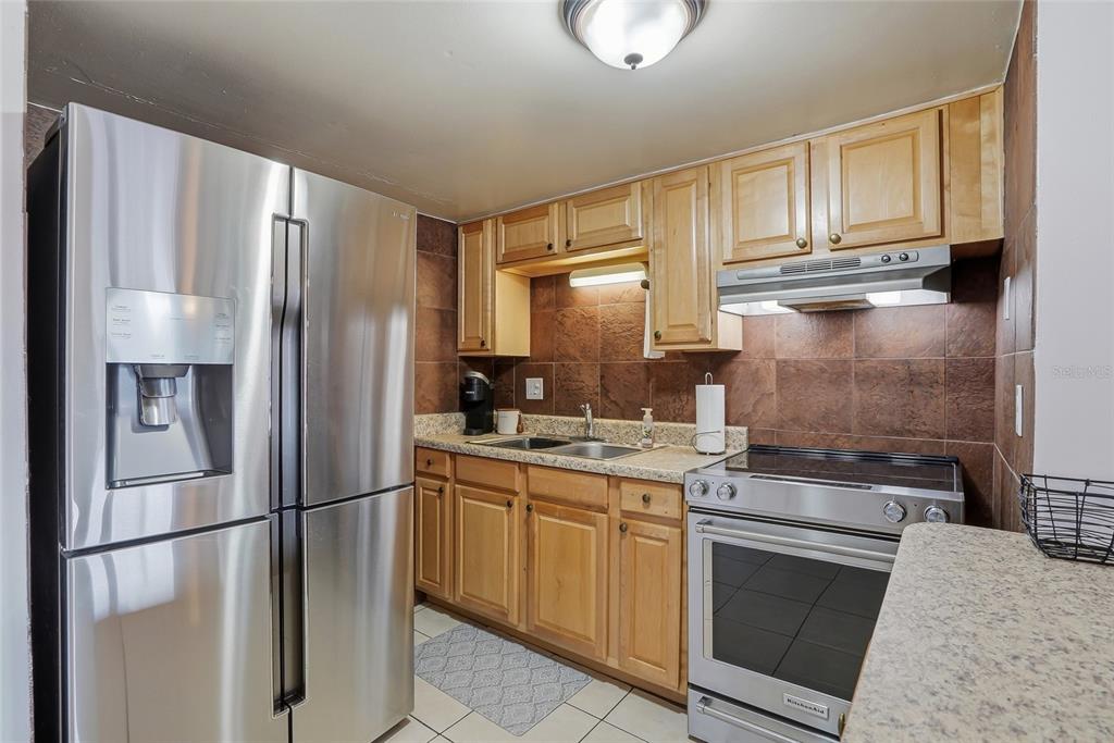 A kitchen features stainless steel appliances, light wood cabinets, and brown tile backsplashes — 8602 CHAMPLAIN COURT UNIT 90, TAMPA, FL