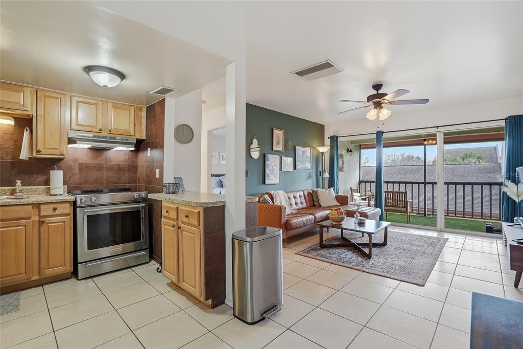 An open-concept kitchen and living area with tile floors, wood cabinets, and a balcony view — 8602 CHAMPLAIN COURT UNIT 90, TAMPA, FL