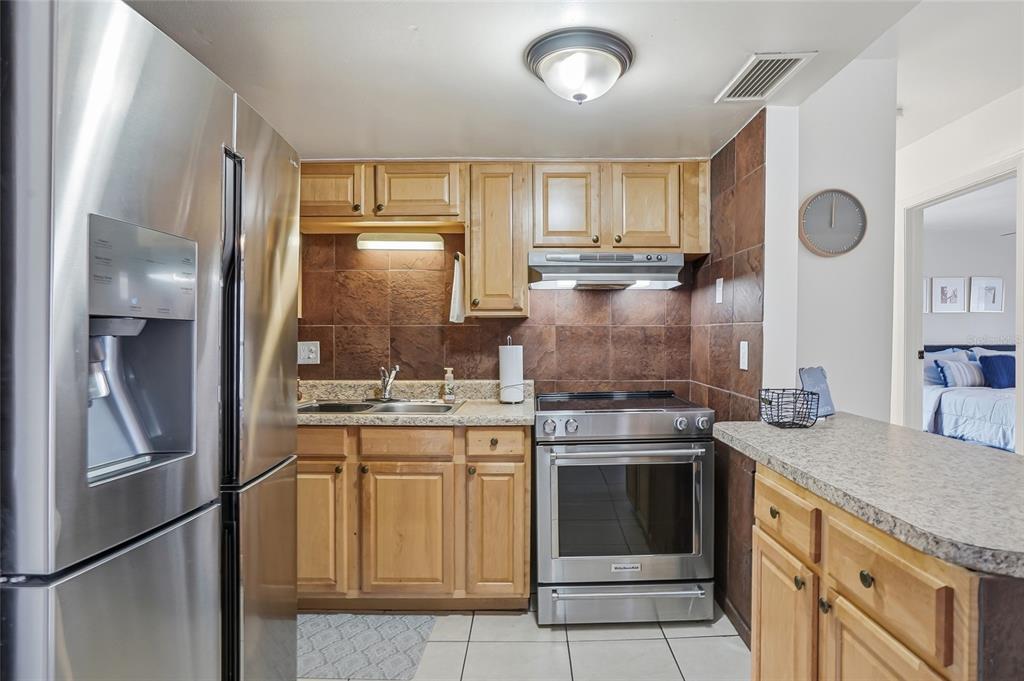 A kitchen with stainless steel appliances, light wood cabinets, and brown tile backsplashes — 8602 CHAMPLAIN COURT UNIT 90, TAMPA, FL