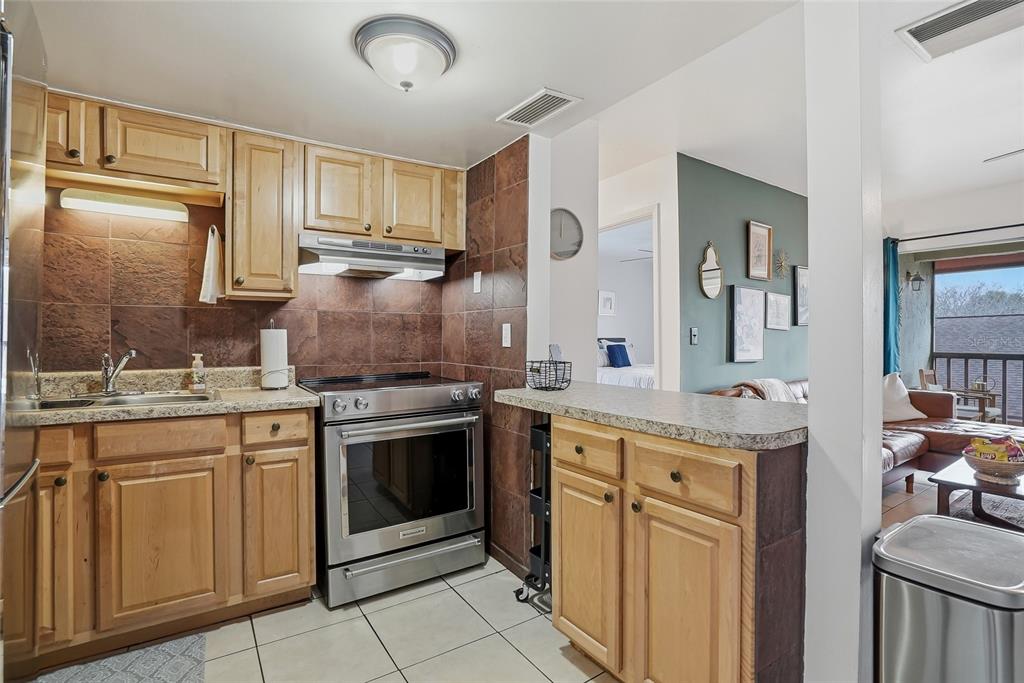 A kitchen with light wood cabinets, stainless steel appliances, and brown tile backsplash — 8602 CHAMPLAIN COURT UNIT 90, TAMPA, FL