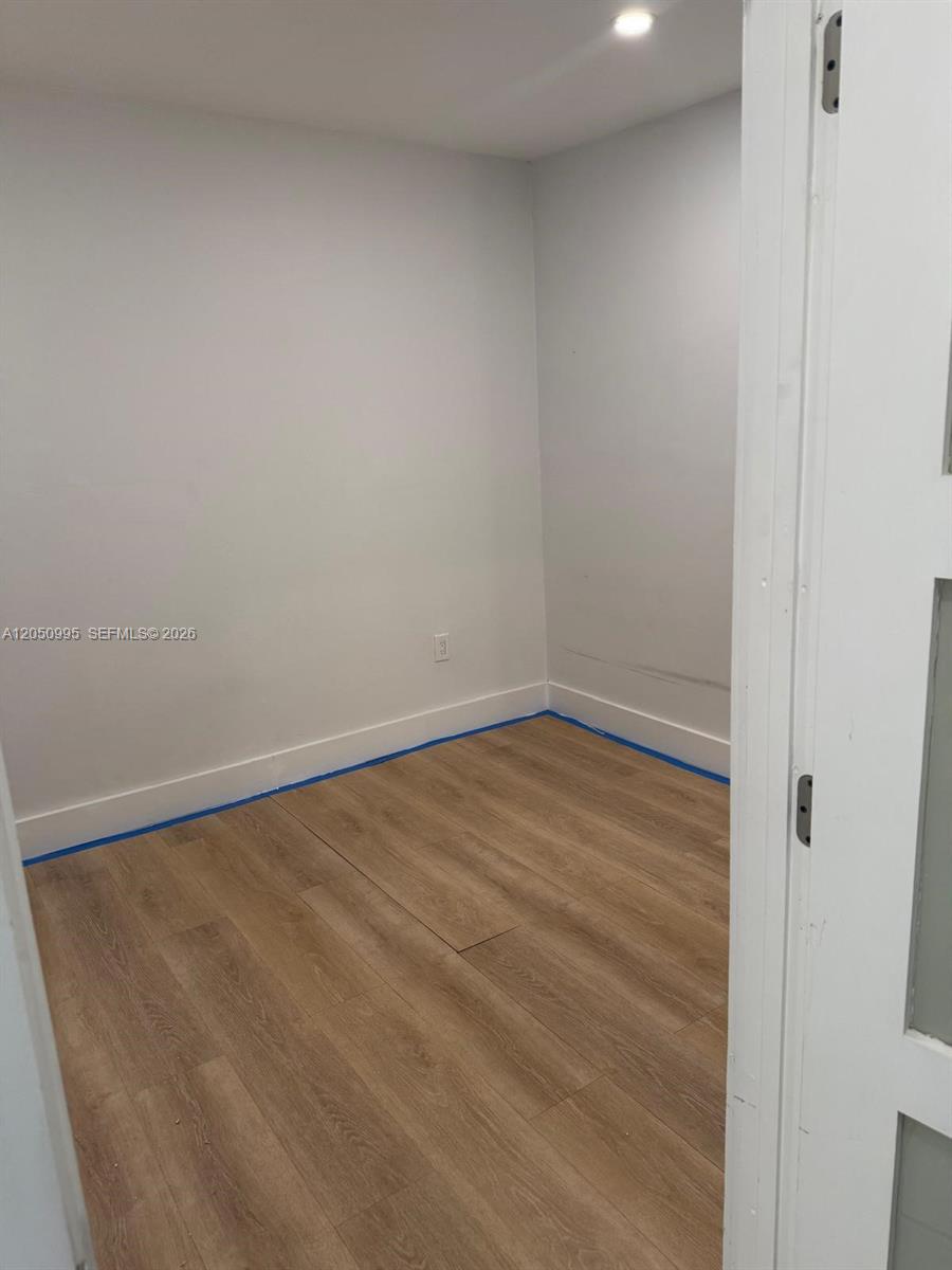 An empty room features light wood-look flooring, white walls, and blue painter's tape along baseboards — 765 W 70th Pl # 1, Hialeah FL 33014, HIALEAH, FL