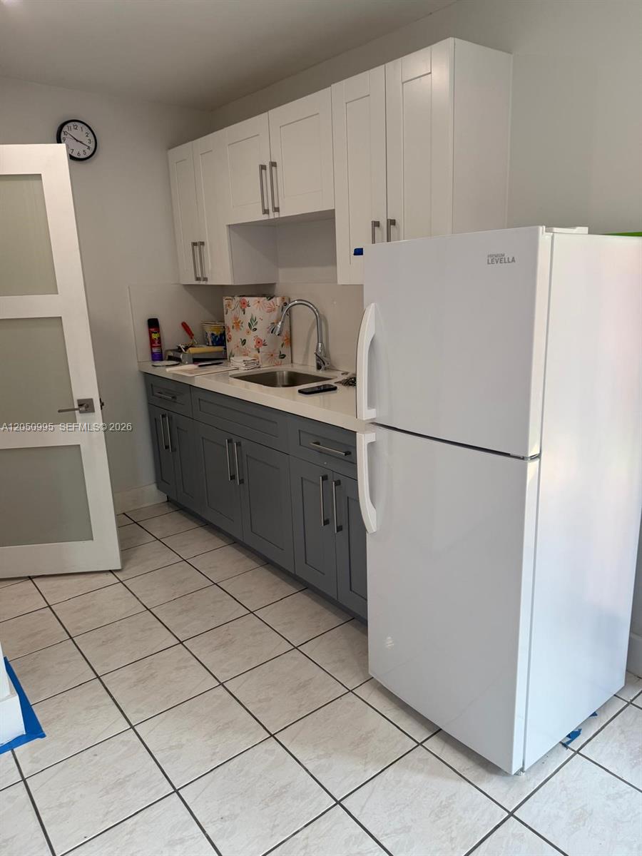 A kitchen features white upper cabinets, gray lower cabinets, a white refrigerator, and tiled flooring — 765 W 70th Pl # 1, Hialeah FL 33014, HIALEAH, FL