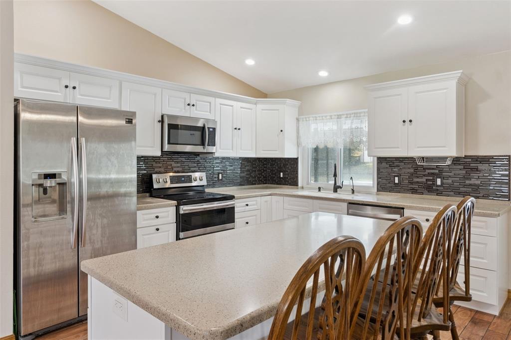 A kitchen with white cabinets, stainless steel appliances, a stone-tiled backsplash, and a central island — 3905 LEMON TREE CT, LAKELAND, FL