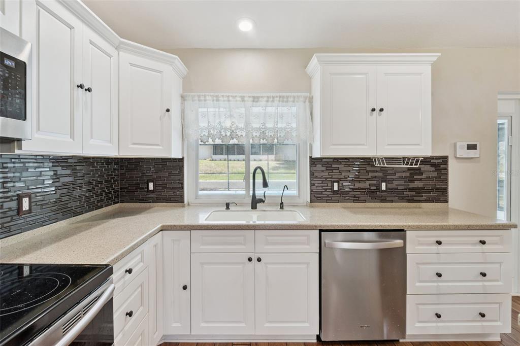 A kitchen with white cabinets, a dark tiled backsplash, stainless steel appliances, and a window — 3905 LEMON TREE CT, LAKELAND, FL