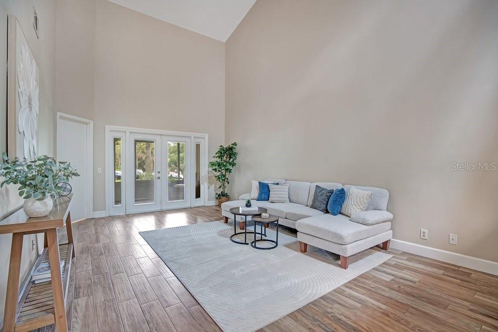 A living room with high ceilings, wood-look tile floors, a sectional sofa, and glass doors — 604 CHESTNUT OAK CIRCLE UNIT 106, ALTAMONTE SPRINGS, FL