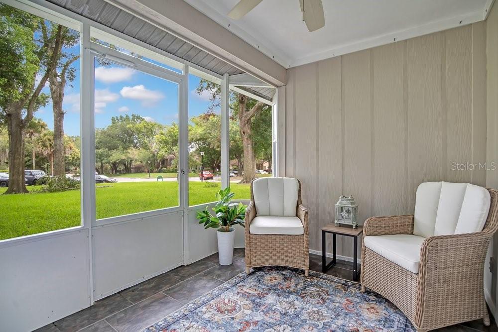 A screened-in porch features tiled flooring, two wicker chairs, and a view of a grassy lawn — 604 CHESTNUT OAK CIRCLE UNIT 106, ALTAMONTE SPRINGS, FL