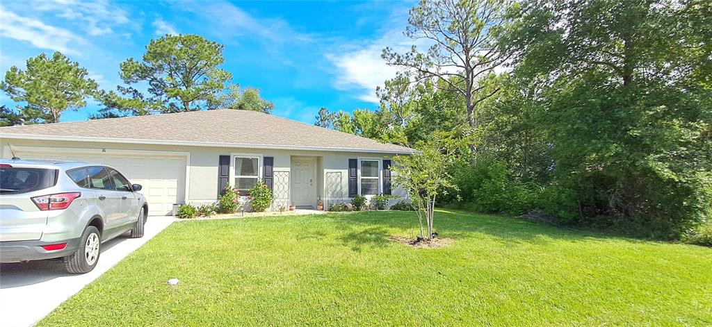 A single-story house with a light-colored exterior, a two-car garage, and a front lawn — 16 PRINCETON LANE, PALM COAST, FL