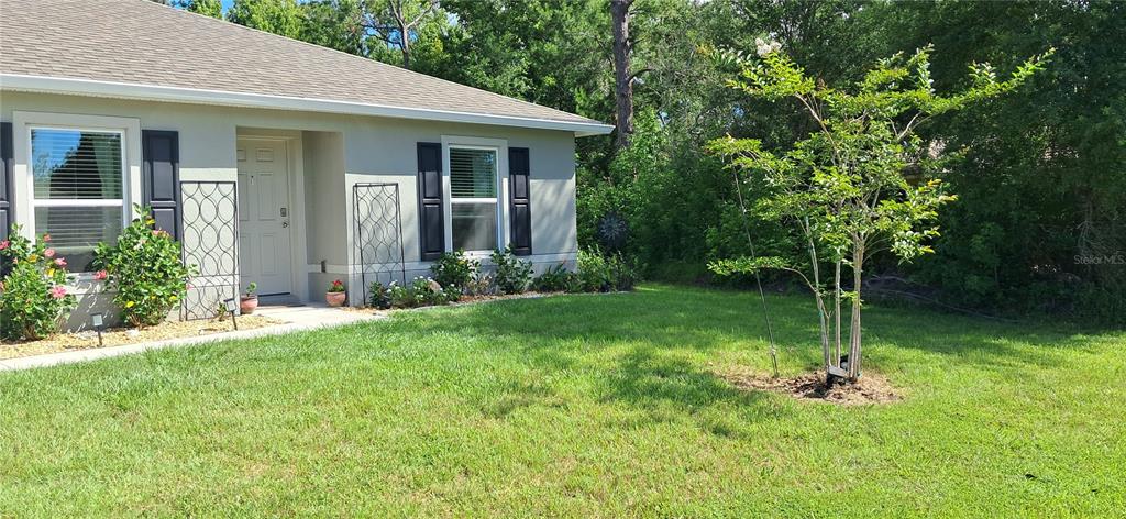 A single-story house exterior features a front entrance, two windows with shutters, and a tree — 16 PRINCETON LANE, PALM COAST, FL