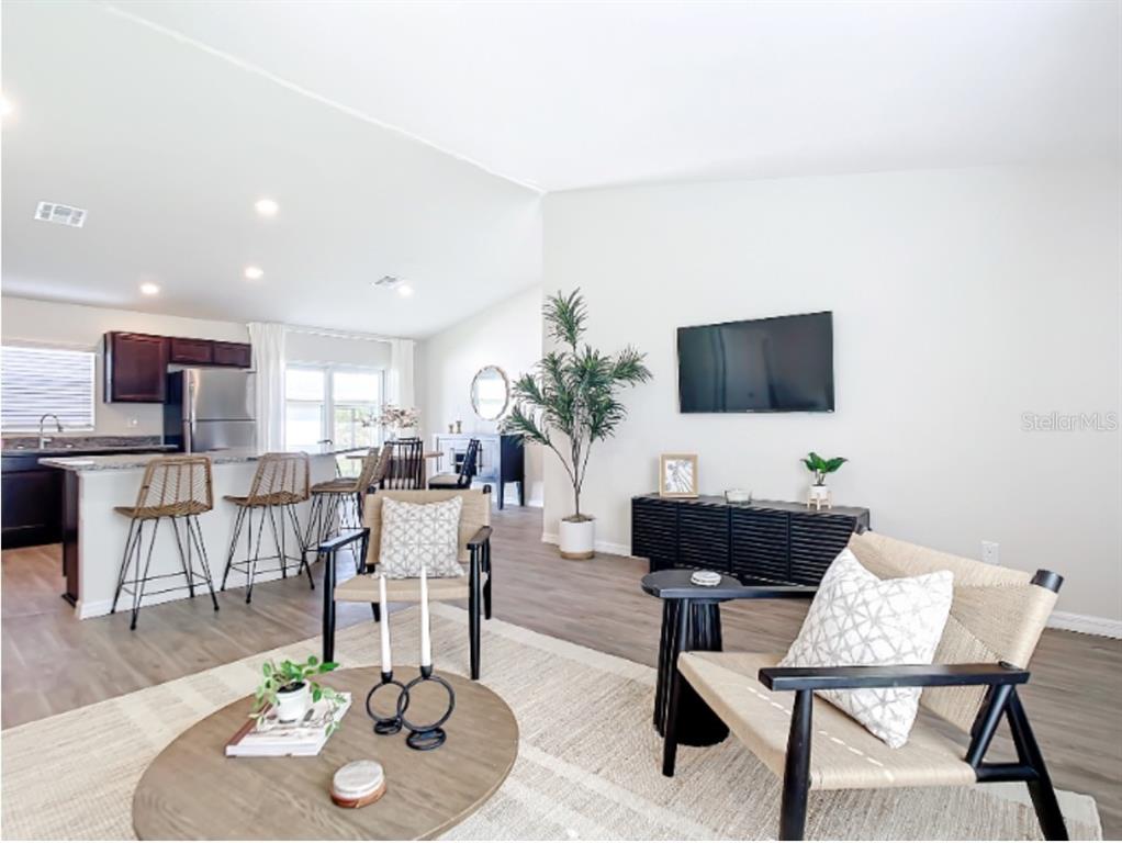 A bright open-concept living room features a kitchen island, wood-look flooring, and modern furniture — 100 PORT ROYAL DRIVE, PALM COAST, FL