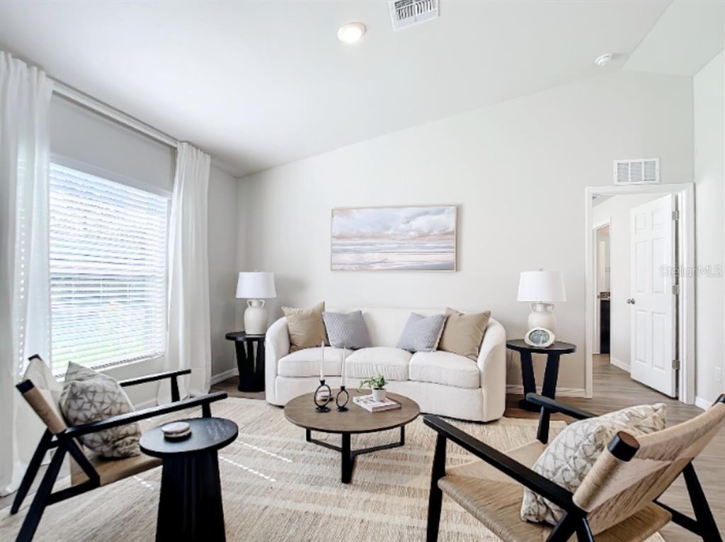 A bright living room features a white sofa, two armchairs, and a round coffee table — 100 PORT ROYAL DRIVE, PALM COAST, FL