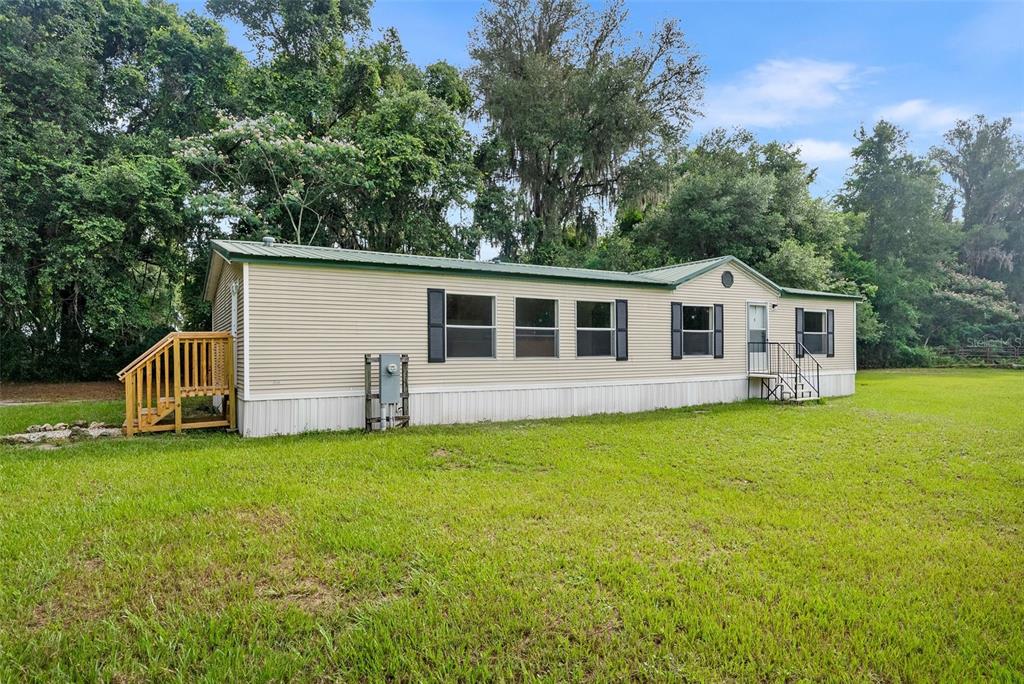 A single-story manufactured home with beige siding sits on a large, grassy lot — 4296 SE COUNTY ROAD 18, LAKE CITY, FL