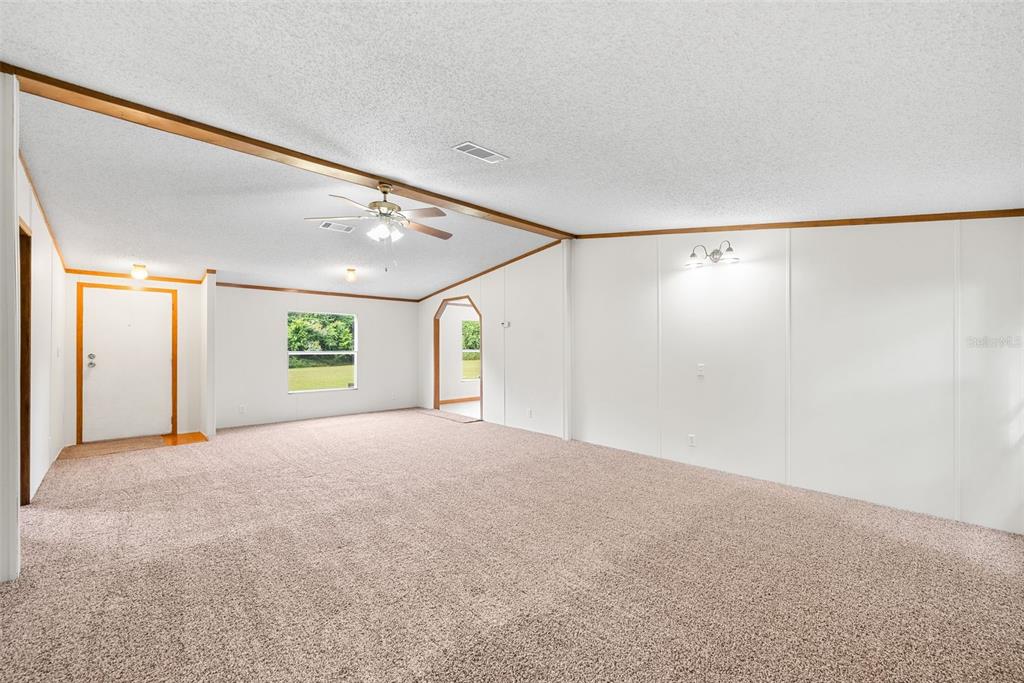 A spacious living room with beige carpet, white walls, a ceiling fan, and wood trim — 4296 SE COUNTY ROAD 18, LAKE CITY, FL
