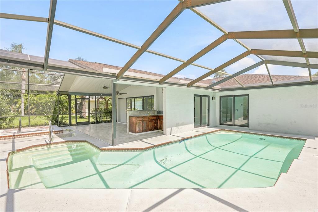 A swimming pool with a tiled edge is enclosed by a screened-in lanai structure — 4509 MITCHER ROAD, NEW PORT RICHEY, FL
