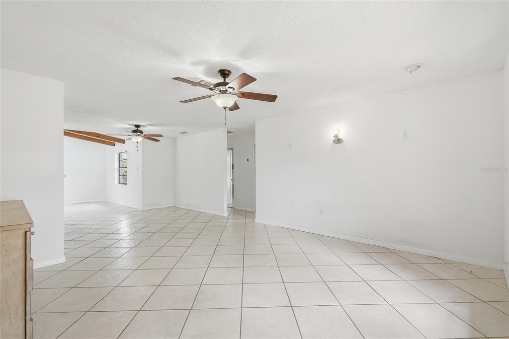 A spacious, white-walled room features light-colored tile flooring and two ceiling fans — 4509 MITCHER ROAD, NEW PORT RICHEY, FL