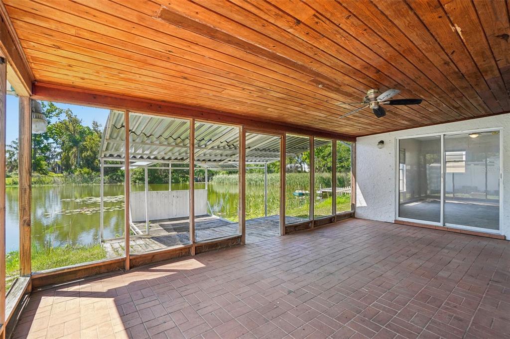 A screened-in porch with a wood-paneled ceiling, brick floor, and a view of a lake — 2024 W SITKA STREET, TAMPA, FL