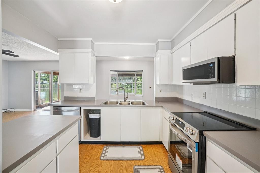 A kitchen with white cabinets, gray countertops, stainless steel appliances, and wood flooring — 2024 W SITKA STREET, TAMPA, FL