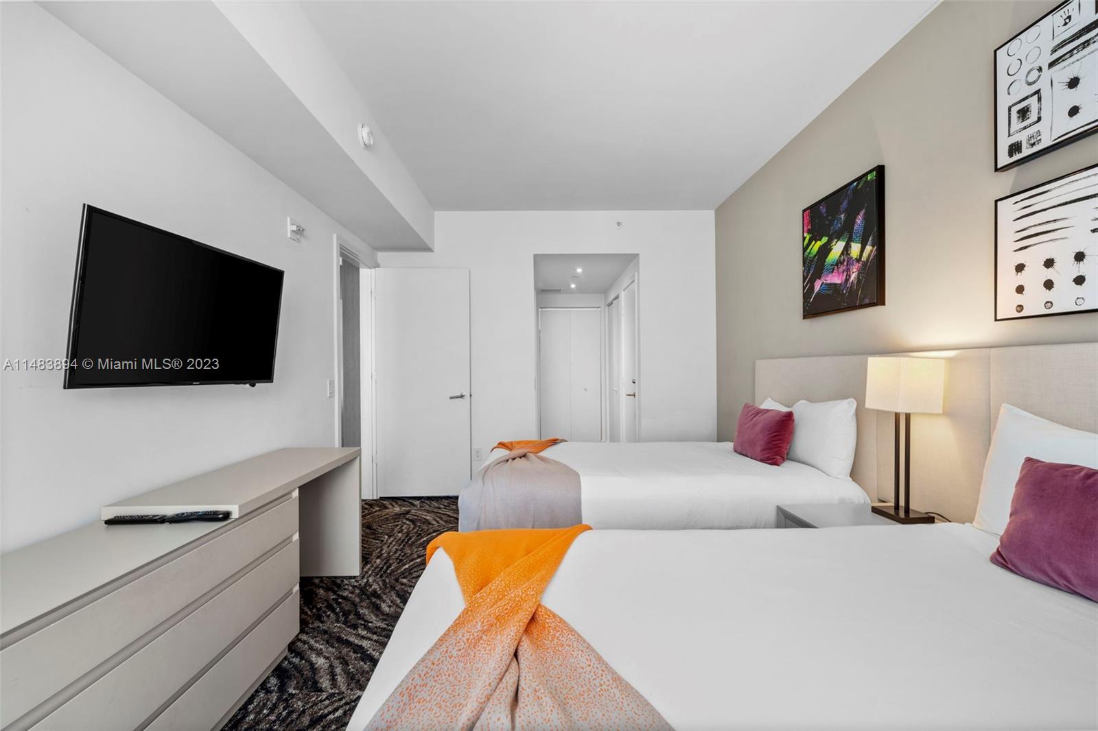 A bedroom features two beds with white linens, orange throws, and a wall-mounted television — 4111 S Ocean Dr # 1406, Hollywood FL 33019, HOLLYWOOD, FL