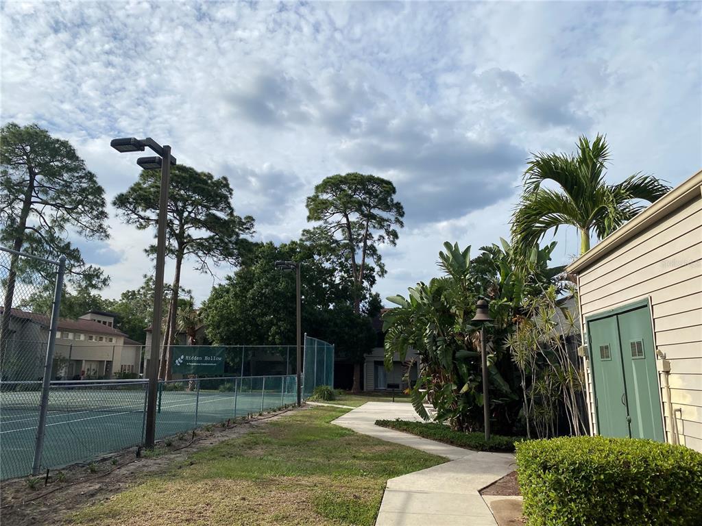 A tennis court sits beside a sidewalk and a building with green double doors — 4394 SANDNER DRIVE, SARASOTA, FL