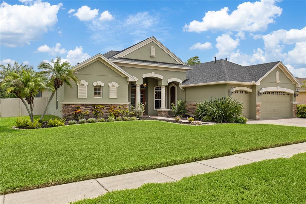 A single-story house with a green stucco exterior, stone accents, and a two-car garage — 3015 LYNWOOD COURT, LAND O LAKES, FL
