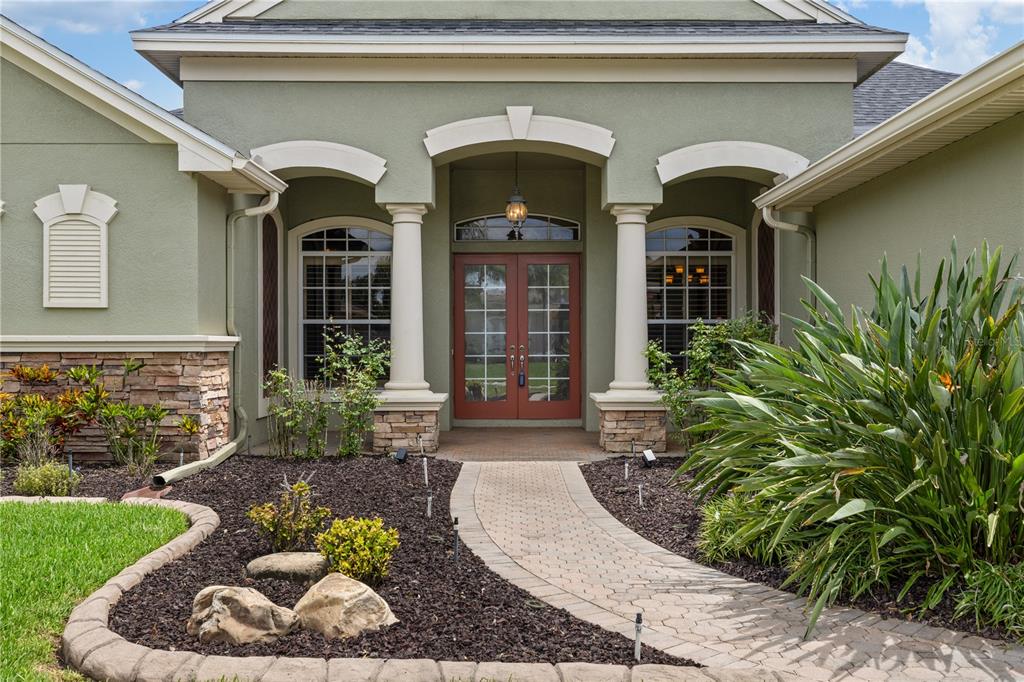 The exterior of a green house features a stone-accented facade, columns, and a paved walkway — 3015 LYNWOOD COURT, LAND O LAKES, FL