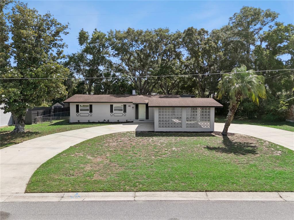 A single-story house with a concrete driveway, breeze block wall, and large trees in front — 1310 LEE COURT, LEESBURG, FL