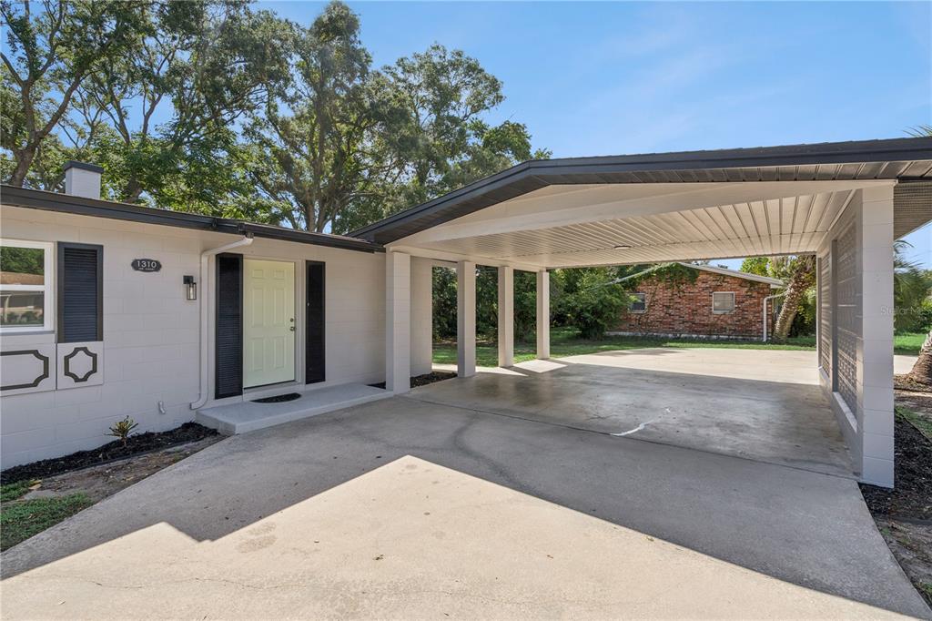 A light-colored house exterior features a concrete driveway leading to a covered carport — 1310 LEE COURT, LEESBURG, FL
