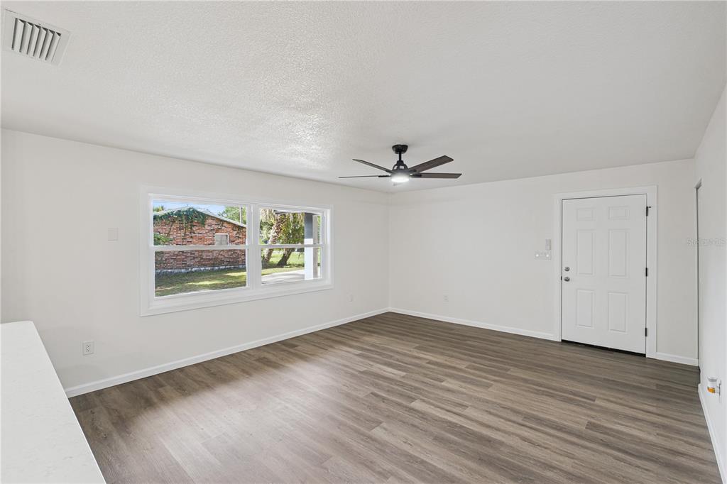 A bright, empty room features white walls, wood-look flooring, a ceiling fan, and a door — 1310 LEE COURT, LEESBURG, FL