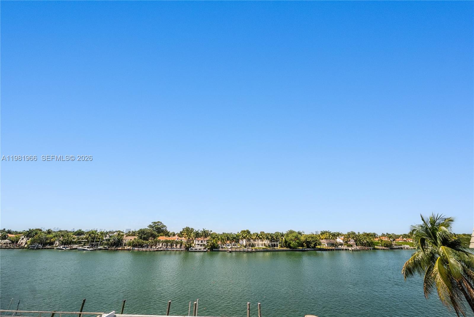 A view of a waterfront residential area with houses, palm trees, and a clear sky — 5750 Collins Ave # 4F, Miami Beach FL 33140, MIAMI BEACH, FL