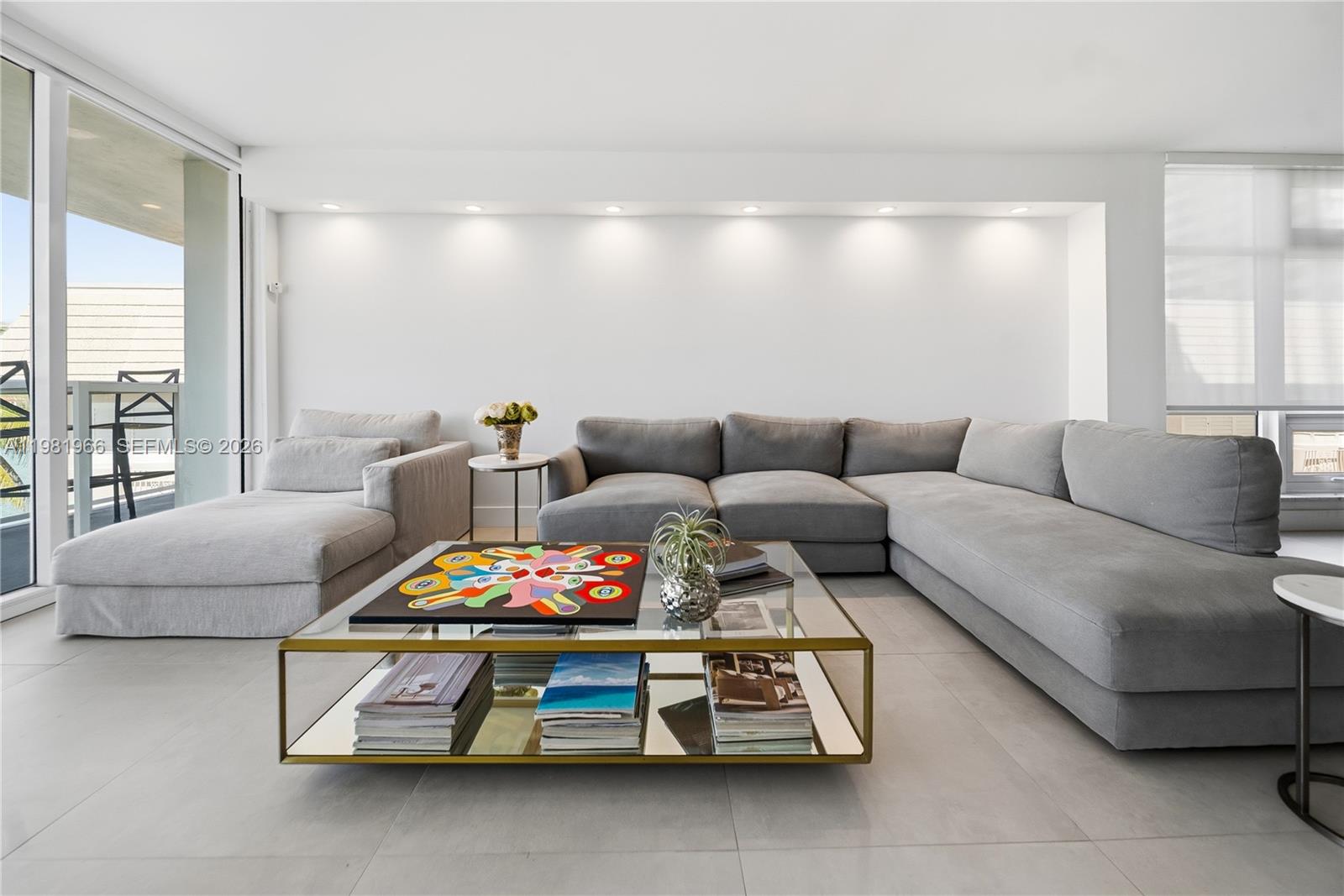 A modern living room features a gray sectional sofa, glass coffee table, and sliding glass doors — 5750 Collins Ave # 4F, Miami Beach FL 33140, MIAMI BEACH, FL