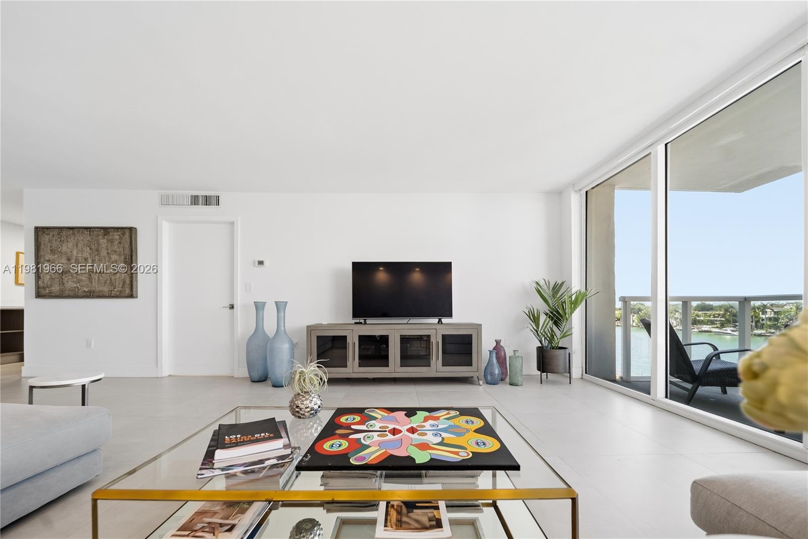 A bright living room features a television console, glass coffee table, and floor-to-ceiling windows — 5750 Collins Ave # 4F, Miami Beach FL 33140, MIAMI BEACH, FL