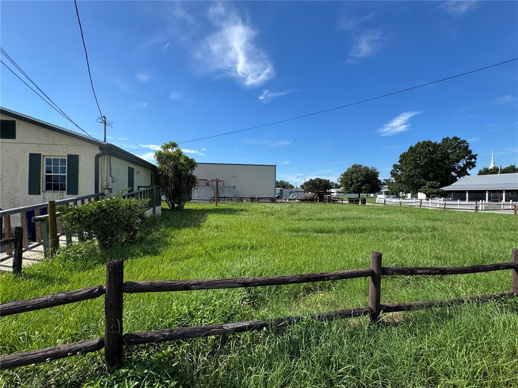 A grassy lot with a wooden fence sits next to a house and metal building — 225 N SCENIC HIGHWAY, FROSTPROOF, FL
