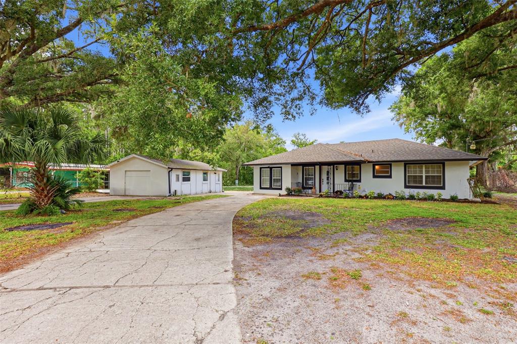 A single-story house with a white exterior, dark trim, and a detached garage under trees — 30151 LYNNE DRIVE, WESLEY CHAPEL, FL