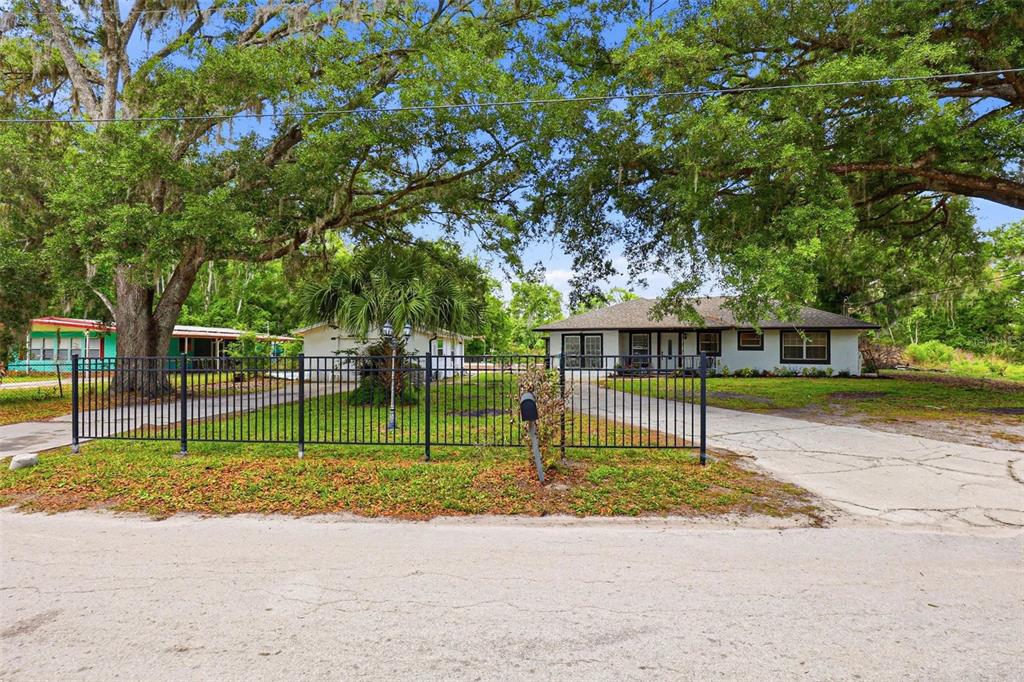 A single-story house with a fenced yard and large oak trees under a blue sky — 30151 LYNNE DRIVE, WESLEY CHAPEL, FL