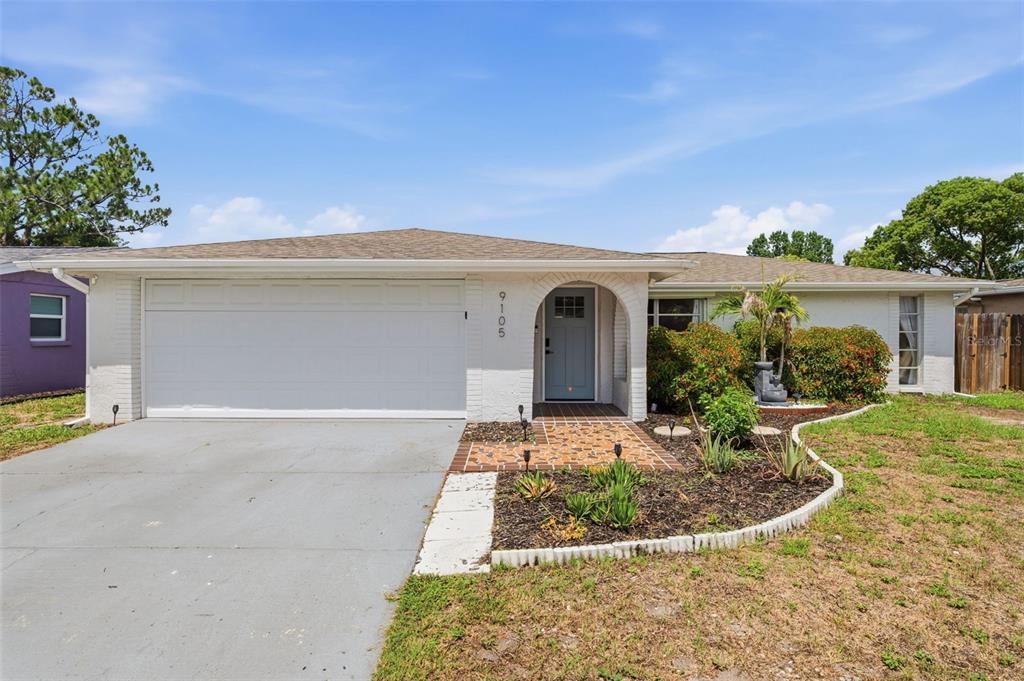 A single-story white brick house features a two-car garage and a blue front door — 9105 HUNT CLUB LANE, PORT RICHEY, FL