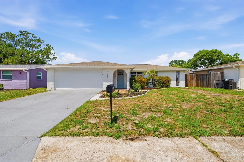 A single-story house with a white exterior, a two-car garage, and a blue front door — 9105 HUNT CLUB LANE, PORT RICHEY, FL