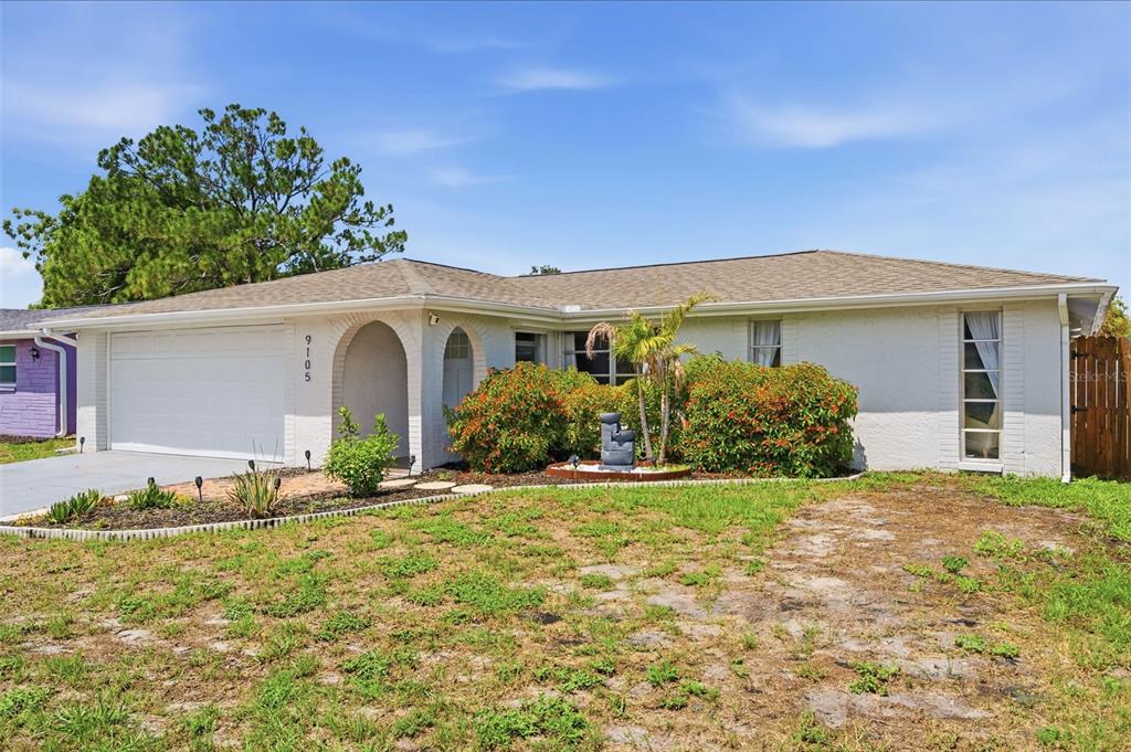 A single-story house with a white brick facade, a two-car garage, and a front lawn — 9105 HUNT CLUB LANE, PORT RICHEY, FL