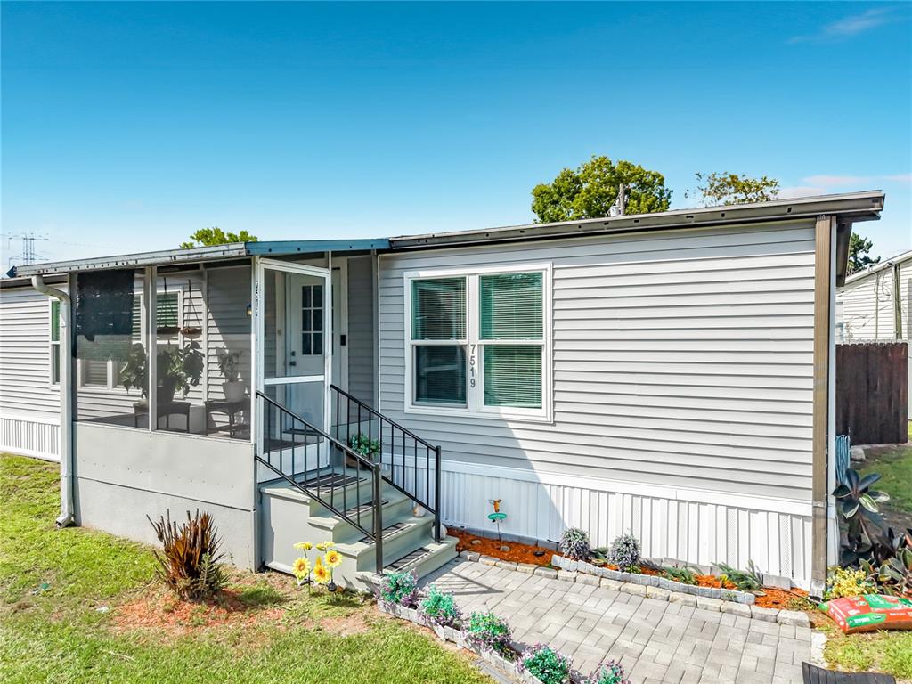 A light gray manufactured home features a screened-in porch, metal stairs, and a paver walkway — 7519 CHARLIN PARKWAY, ORLANDO, FL