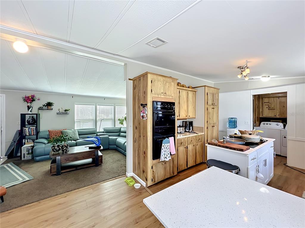 A kitchen with wooden cabinets and a white island overlooks a living room with furniture — 7519 CHARLIN PARKWAY, ORLANDO, FL