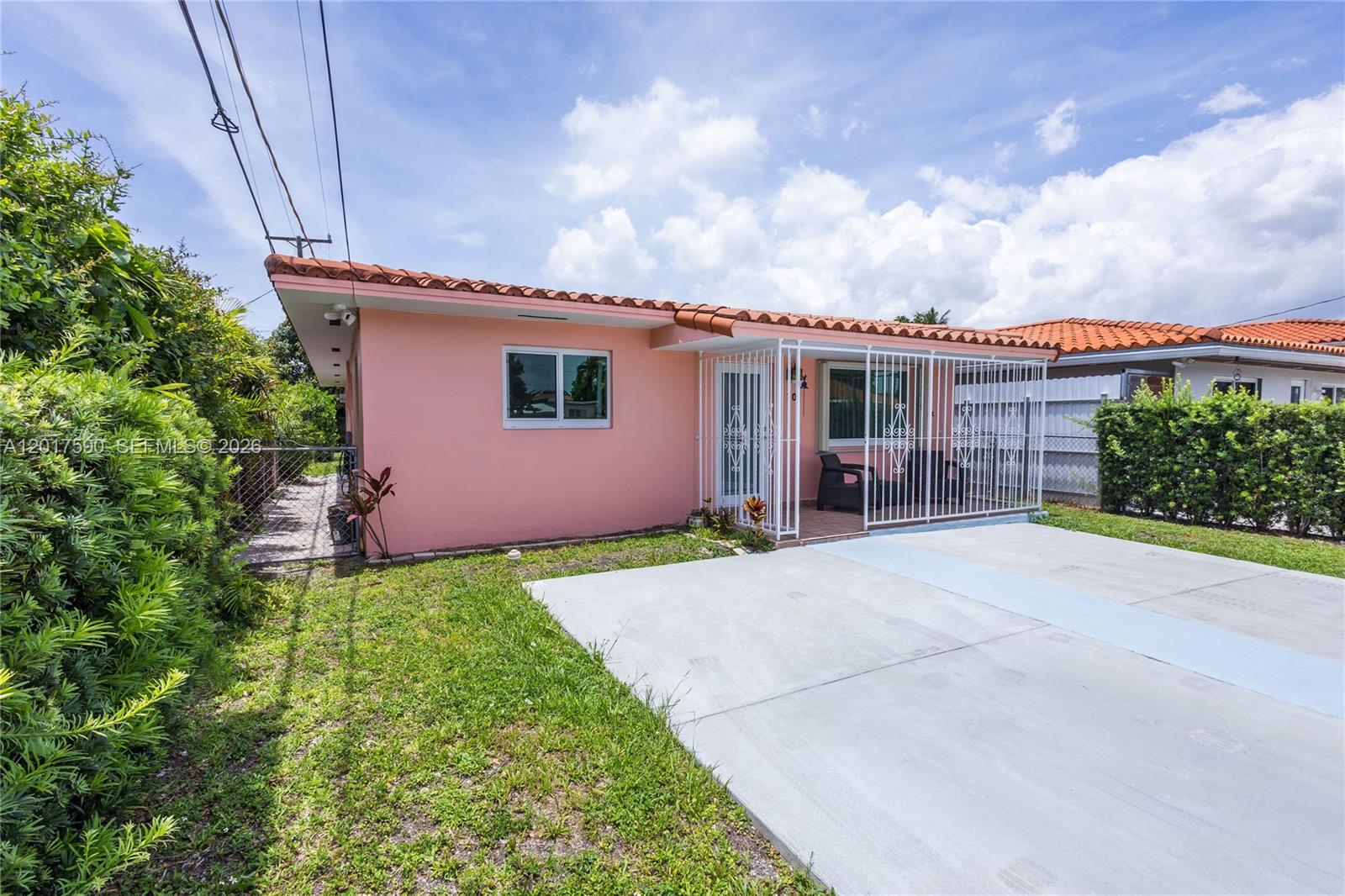 A pink single-story house features a tiled roof, a concrete driveway, and a gated porch — 10 NW 60th Ct, Miami FL 33126, MIAMI, FL