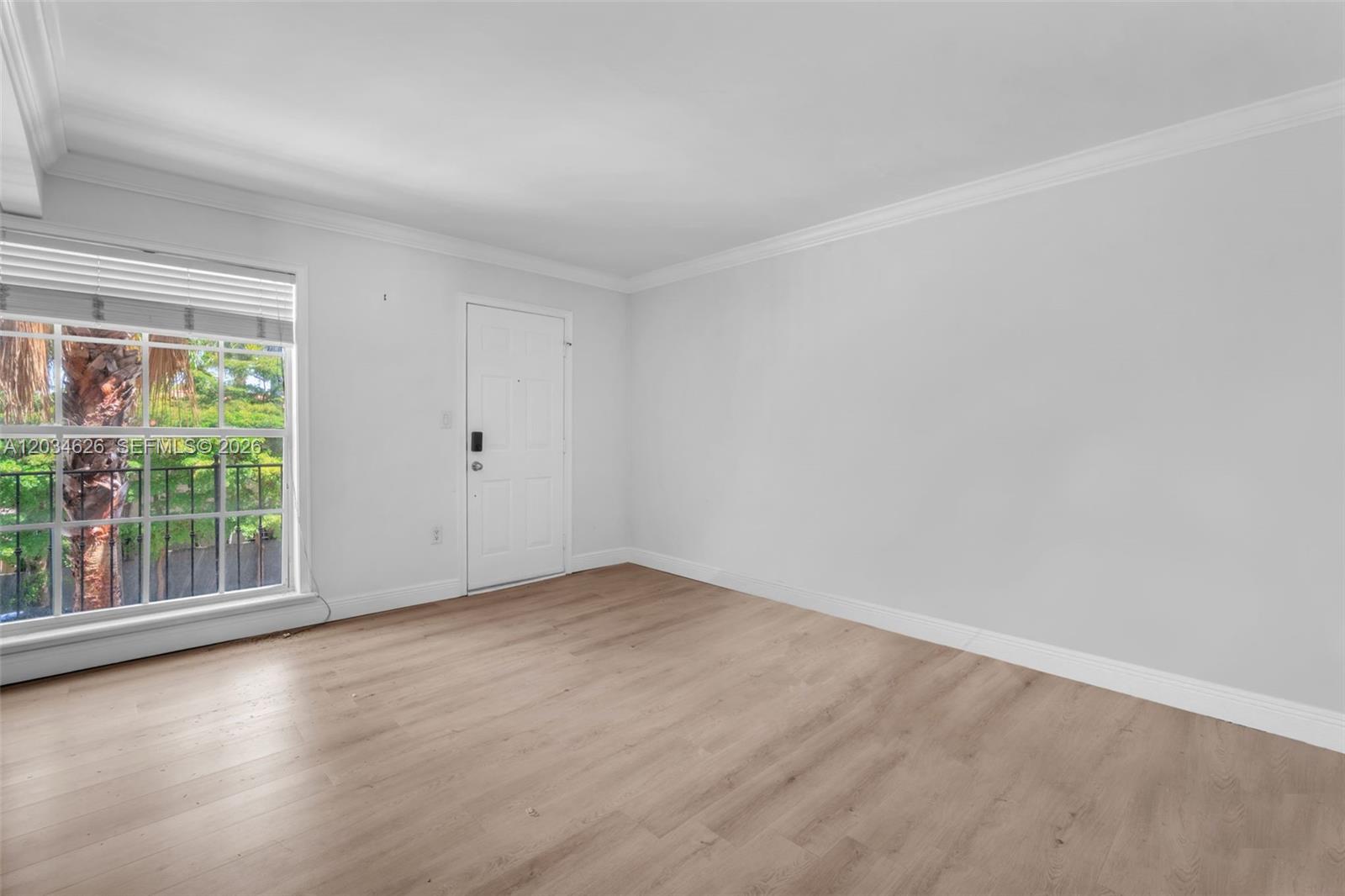 An empty room features light wood-look flooring, white walls, crown molding, and a window — 3245 Virginia St # 48, Miami FL 33133, MIAMI, FL