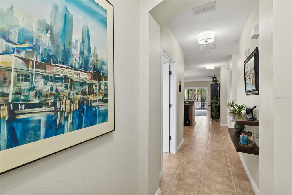 A hallway with tile flooring, wall art, and floating shelves leads toward a living area — 100 CANOPY WALK LANE UNIT 124, PALM COAST, FL