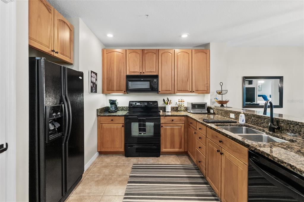 A kitchen features wood cabinets, black appliances, granite countertops, and a striped floor rug — 100 CANOPY WALK LANE UNIT 124, PALM COAST, FL