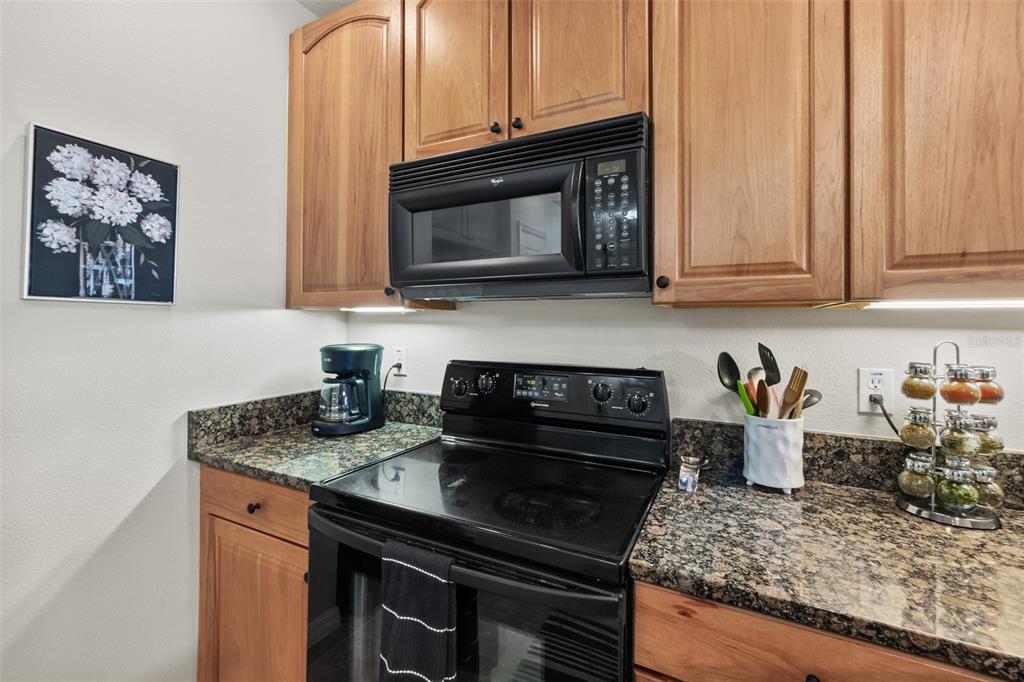 A kitchen features wood cabinets, granite countertops, and black appliances including a stove and microwave — 100 CANOPY WALK LANE UNIT 124, PALM COAST, FL