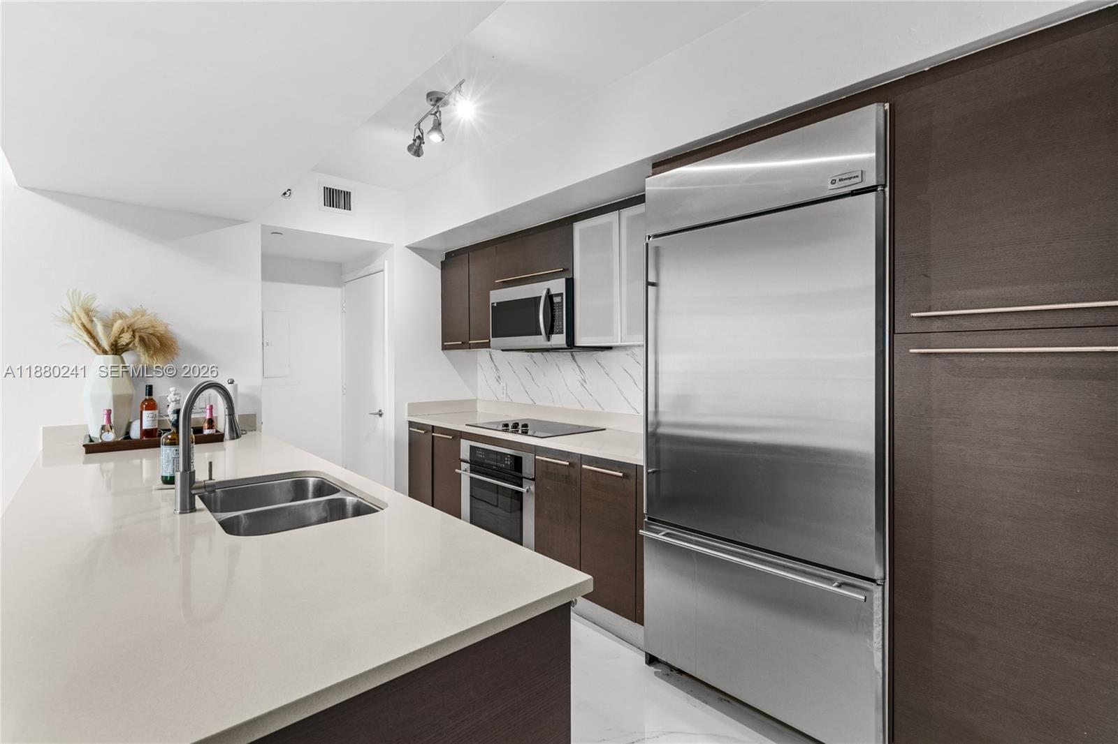 A modern kitchen features dark wood cabinetry, stainless steel appliances, and a white quartz island — 55 SE 6th St # 1203, Miami FL 33131, MIAMI, FL