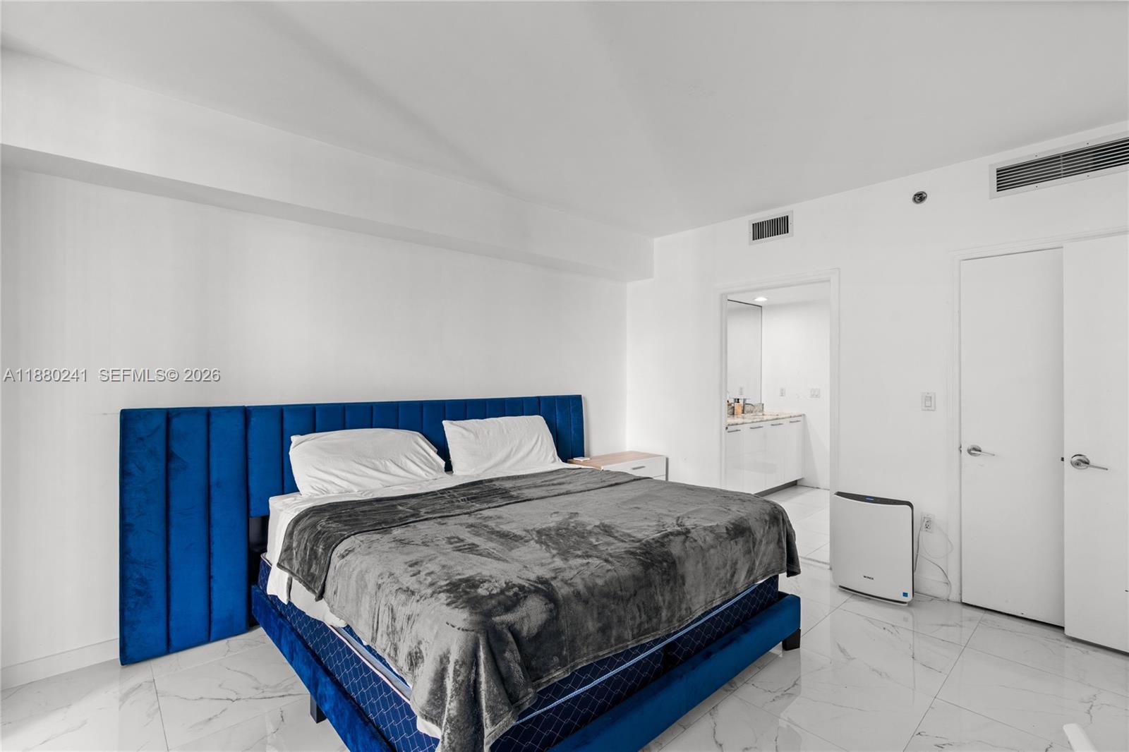 A bedroom features a blue velvet bed, white walls, and white marble-style flooring — 55 SE 6th St # 1203, Miami FL 33131, MIAMI, FL