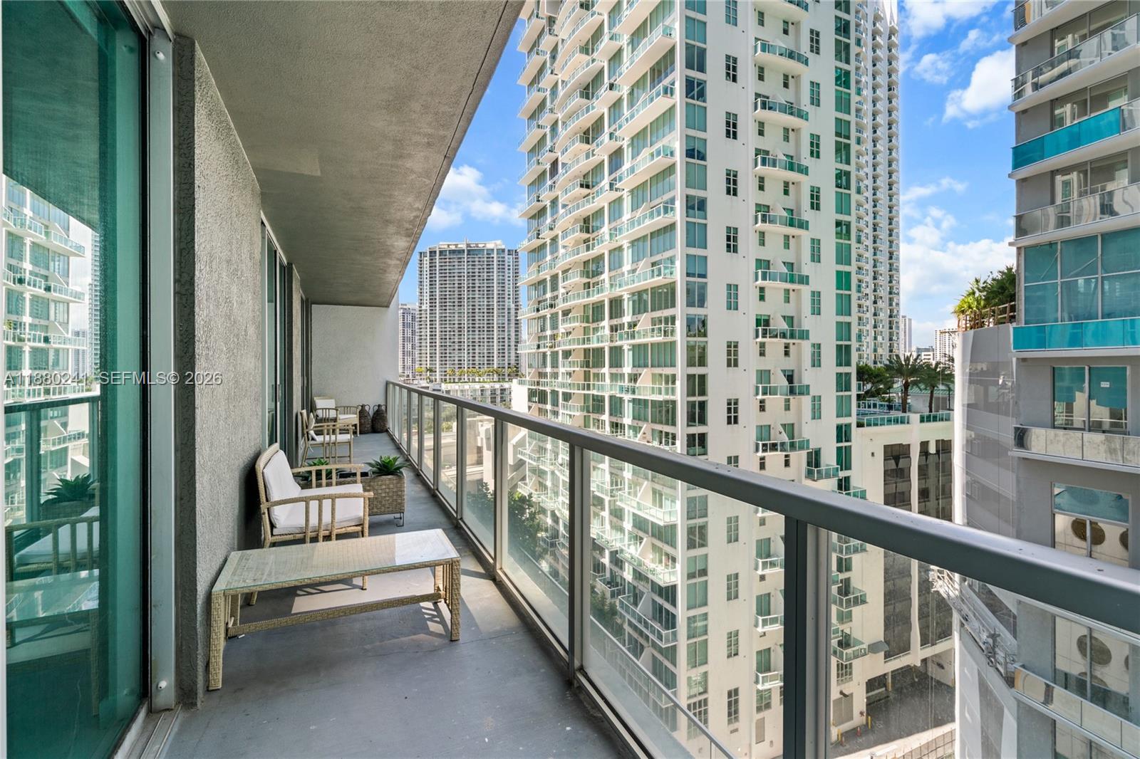 A balcony with outdoor furniture overlooks a dense urban skyline of high-rise apartment buildings — 55 SE 6th St # 1203, Miami FL 33131, MIAMI, FL