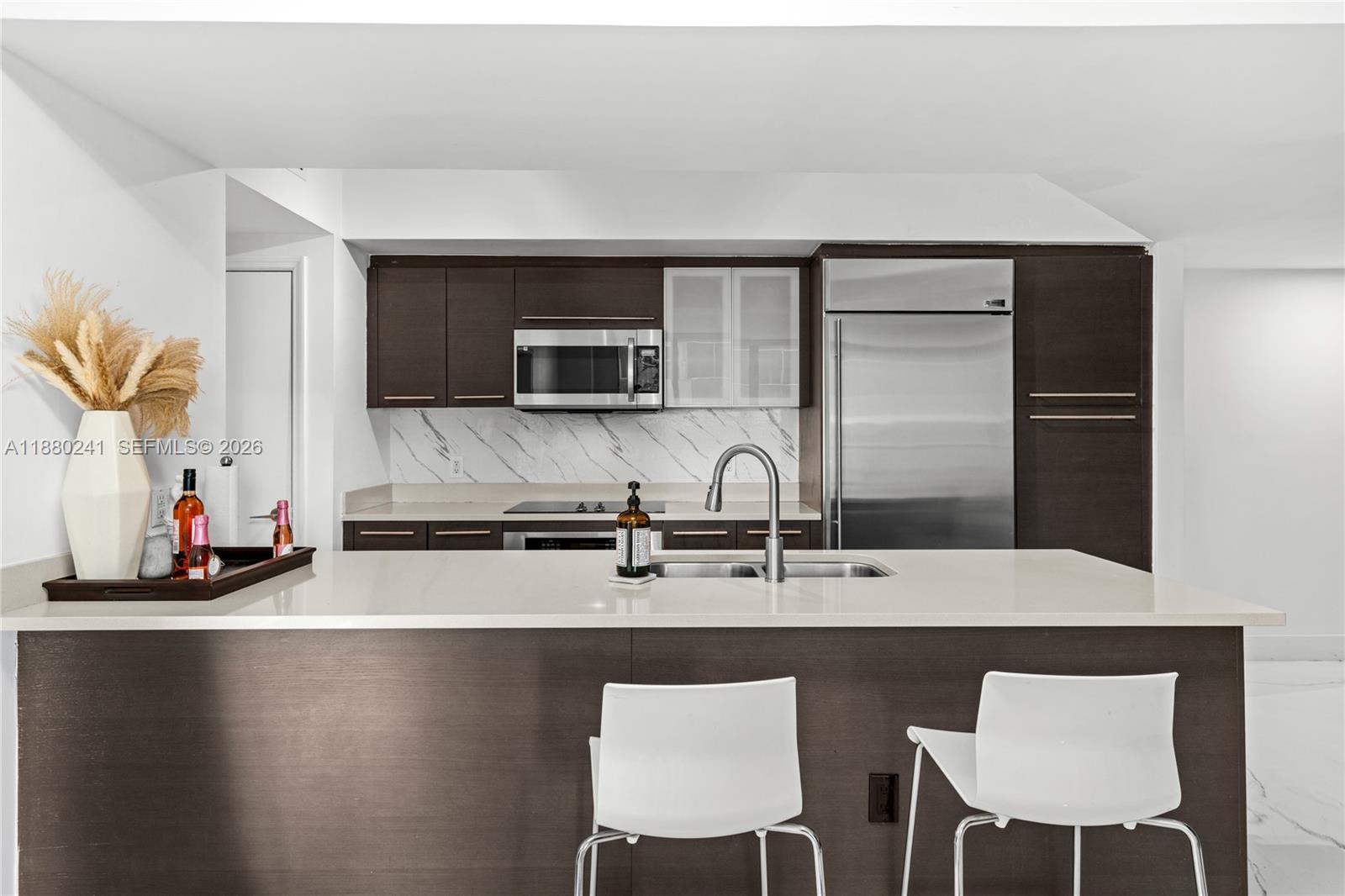 A modern kitchen features dark wood cabinetry, stainless steel appliances, and a white quartz island — 55 SE 6th St # 1203, Miami FL 33131, MIAMI, FL
